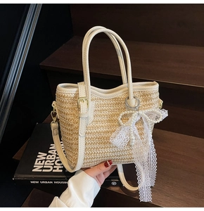 Detail of hand-woven straw bucket bag with lace bow, pearl charm, and leather handles