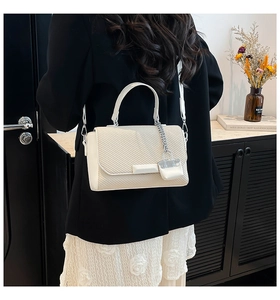 Rear view of model wearing a beige woven square handbag with a mini bag charm and strap