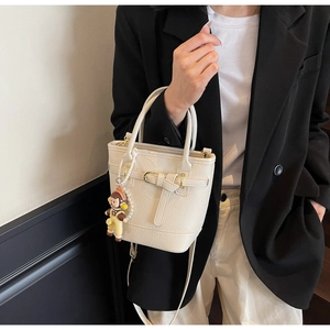 Detail of cream white litchi texture bucket bag with decorative buckle and cute doll charm