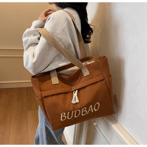 Detailed view of the brown canvas tote bag with BUDBAO embroidery and cotton tassels