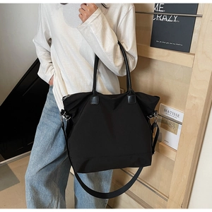 Détail du sac fourre-tout noir en nylon avec poignées en cuir et bandoulière amovible en lumière