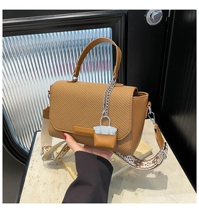 Detail of brown leather handbag featuring a woven flap and ethnic style wide shoulder strap
