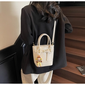 Detailed view of creamy white litchi textured bucket bag with cute doll charm accessory