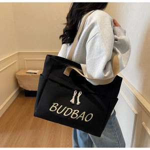 Detail of black canvas tote bag with contrast cream straps and BUDBAO embroidery on side