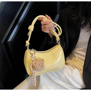 Detail showing the light yellow crescent bag with its brown plush bear charm and woven cord