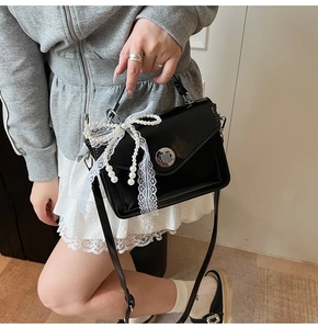 Détail d'un sac à main noir en cuir ciré avec nœud en dentelle et pompon perlé