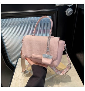 Detail of pink woven handbag with leather flap, geometric strap, and chain charm