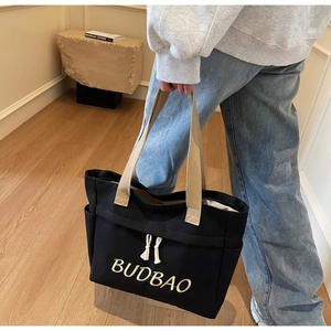 Detail of black canvas tote bag with BUDBAO embroidery and cotton rope tassels
