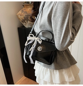 Détail du sac bandoulière en cuir noir huilé avec chaîne de perles et nœud en dentelle