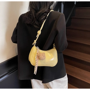 Detail of yellow patent leather shoulder bag with plush bear charm and tassel ornament