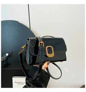 Détail d'un sac bandoulière en cuir verni noir avec une boucle carrée en métal doré