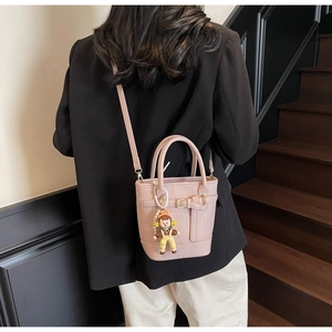 Pink lychee texture bucket bag with cute doll pendant shown on a modern staircase