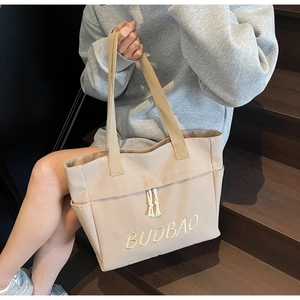 Close-up of beige canvas tote bag with yellow BUDBAO embroidery and white knot detail
