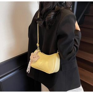 Close-up of light yellow crescent shoulder bag featuring a cute plush bear charm and silk ribbon
