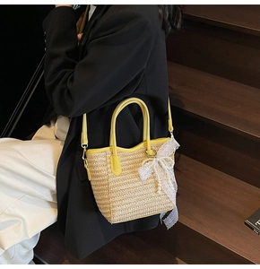 Detail of straw bucket bag featuring yellow leather handles and white lace bow with pearls