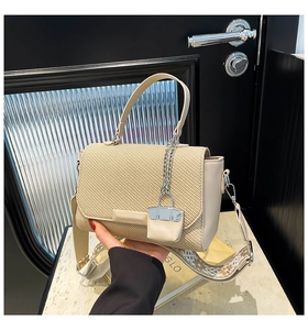 Detail of beige woven handbag with embroidered wide strap and silver chain charm accessory