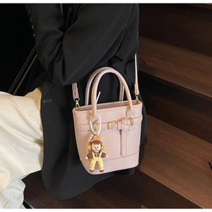 Close-up of pink litchi grain leather bucket bag with cute cartoon charm on a model