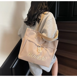 Detail of beige canvas tote bag with yellow BUDBAO embroidery and cotton tassel accents
