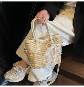Detail view of woven straw bucket bag with lace bow pendant and leather strap