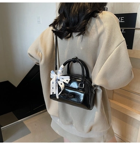 Detail of black patent leather Boston bag featuring a bow and floral scarf on the handle