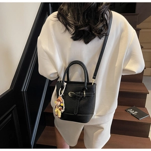 Detail of black lychee grain bucket bag with golden buckle and pearl girl charm accessory