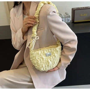 Detail of light yellow pleated cloud bag with metallic logo on a stylish shoulder strap