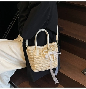 Detail of woven straw bucket bag with white lace bow, pearls, and leather trim handle
