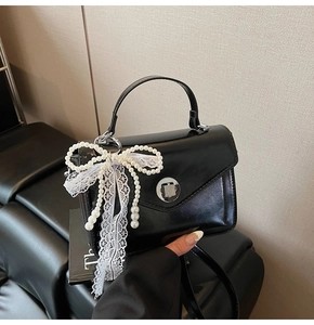Détail du sac à main noir en cuir ciré avec nœud en dentelle perlée et fermoir argenté