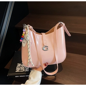 Detail of a pink patent leather shoulder bag with a silver G-buckle and colorful charms
