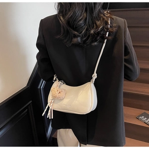 Detail showing creamy white shoulder bag with plush bear charm and striped ribbon accent