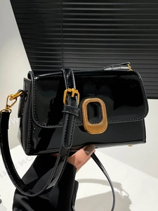 Sac bandoulière élégant en cuir verni noir avec boucle dorée sur un support blanc pur