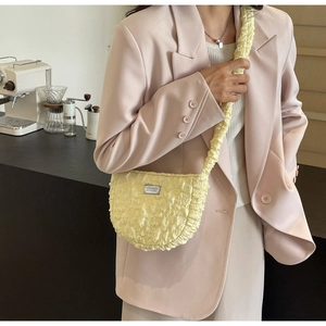 Detail of light yellow ruched cloud bag with silver logo plate worn with a pink blazer