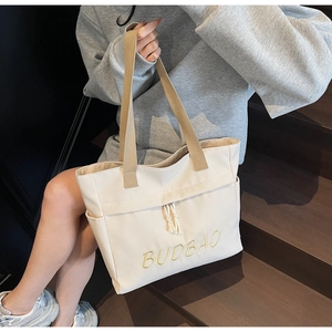 Detail of cream canvas tote bag showing BUDBAO embroidery and side pocket feature
