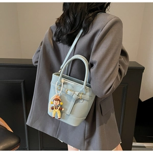 Detail of light blue lychee texture bucket bag with cartoon pendant on grey blazer