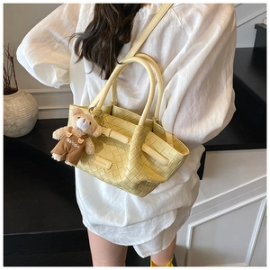 Detail of light yellow woven leather bag with a cute bear pendant on a staircase