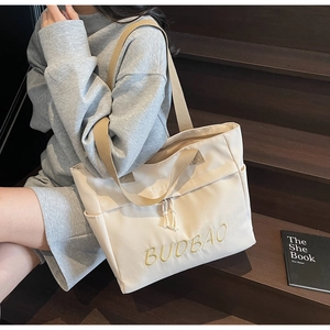 Detail view of large canvas tote bag with embroidered letters on a wooden staircase