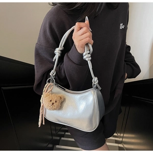 Detail of silver patent leather shoulder bag with decorative strap knot and bear charm