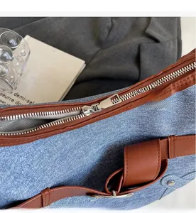 Détail du sac en denim bleu clair avec bandoulière en cuir marron et fermeture éclair