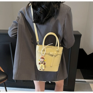 Detail of yellow bucket bag with lychee texture and a cute cartoon charm on suit