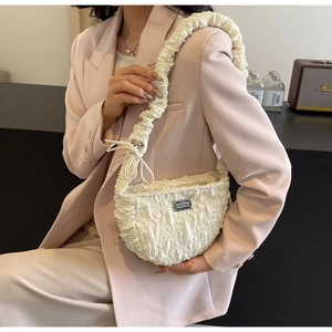 Close-up of cream-colored pleated shoulder bag with delicate fabric folds and silver metal logo