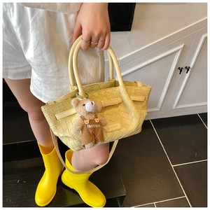 Detail of yellow woven bucket bag with cute bear charm and adjustable shoulder strap