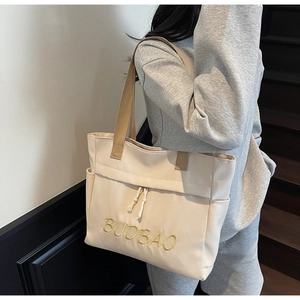 Detail of beige canvas tote bag showing yellow BUDBAO embroidery and drawstring pocket