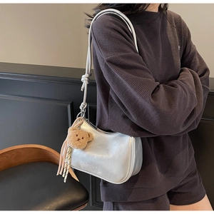 Detail of silver metallic shoulder bag featuring brown bear plush charm and tassel detail
