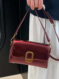 Sac bandoulière rétro en cuir verni bordeaux avec boucle dorée porté par un mannequin