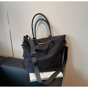 Détail d'un grand sac fourre-tout noir en nylon avec poignées en cuir sur sofa