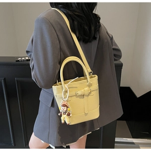 Detail of yellow lychee texture bucket bag with metal buckle and cute girl charm