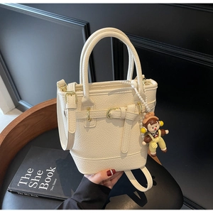 Detail of white lychee leather bucket bag featuring gold hardware and a cute charm