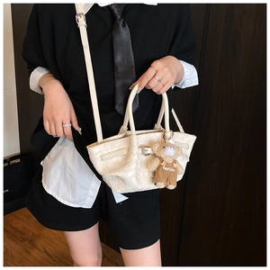 Close-up of white woven bucket bag with decorative buckle strap and plush bear charm
