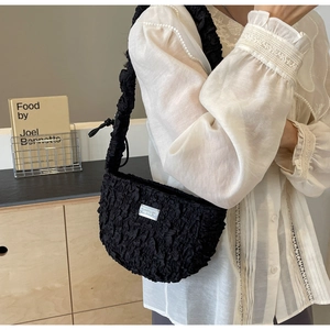Detail shot of black scrunchie texture shoulder bag with rectangular silver logo plaque