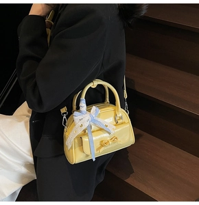 Detail of a bright yellow mini Boston bag featuring a bow pocket and plaid ribbon decor